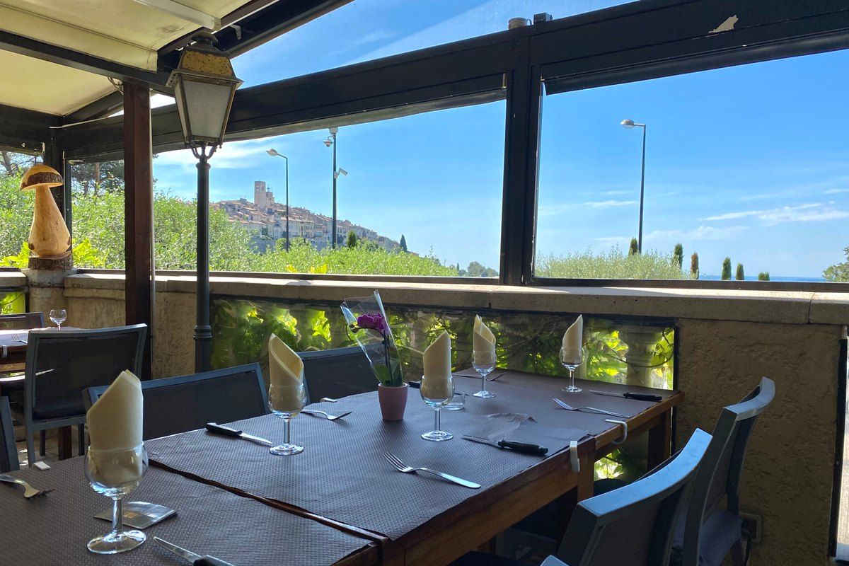 Glassed-in terrace tables at La Terrasse sur Saint-Paul with the walled village on the hill beyond