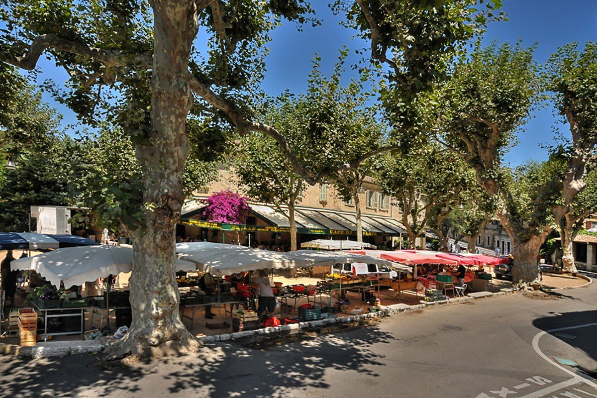 Market stalls under the plane trees of Place de Gaulle at the entrance to Saint-Paul de Vence