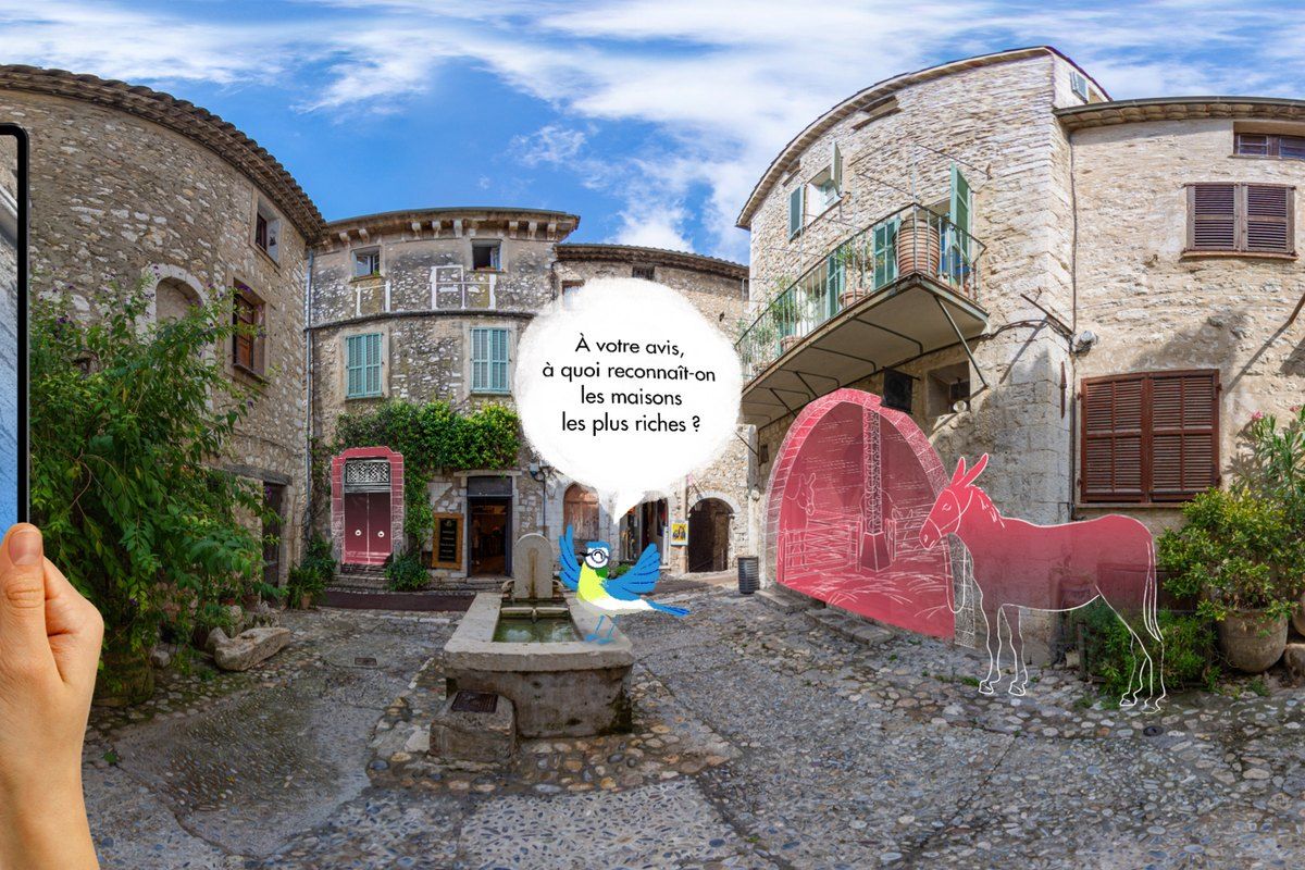 A tablet held up in a Saint-Paul de Vence square shows the augmented-reality tour with Rémy the blue tit