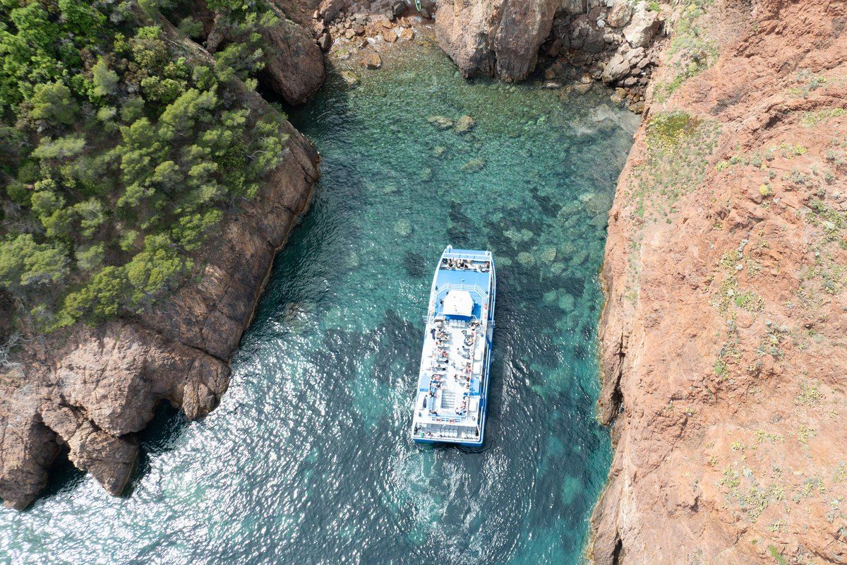 A Bateaux Bleus boat seen from above in a turquoise calanque between the red rocks of the Estérel