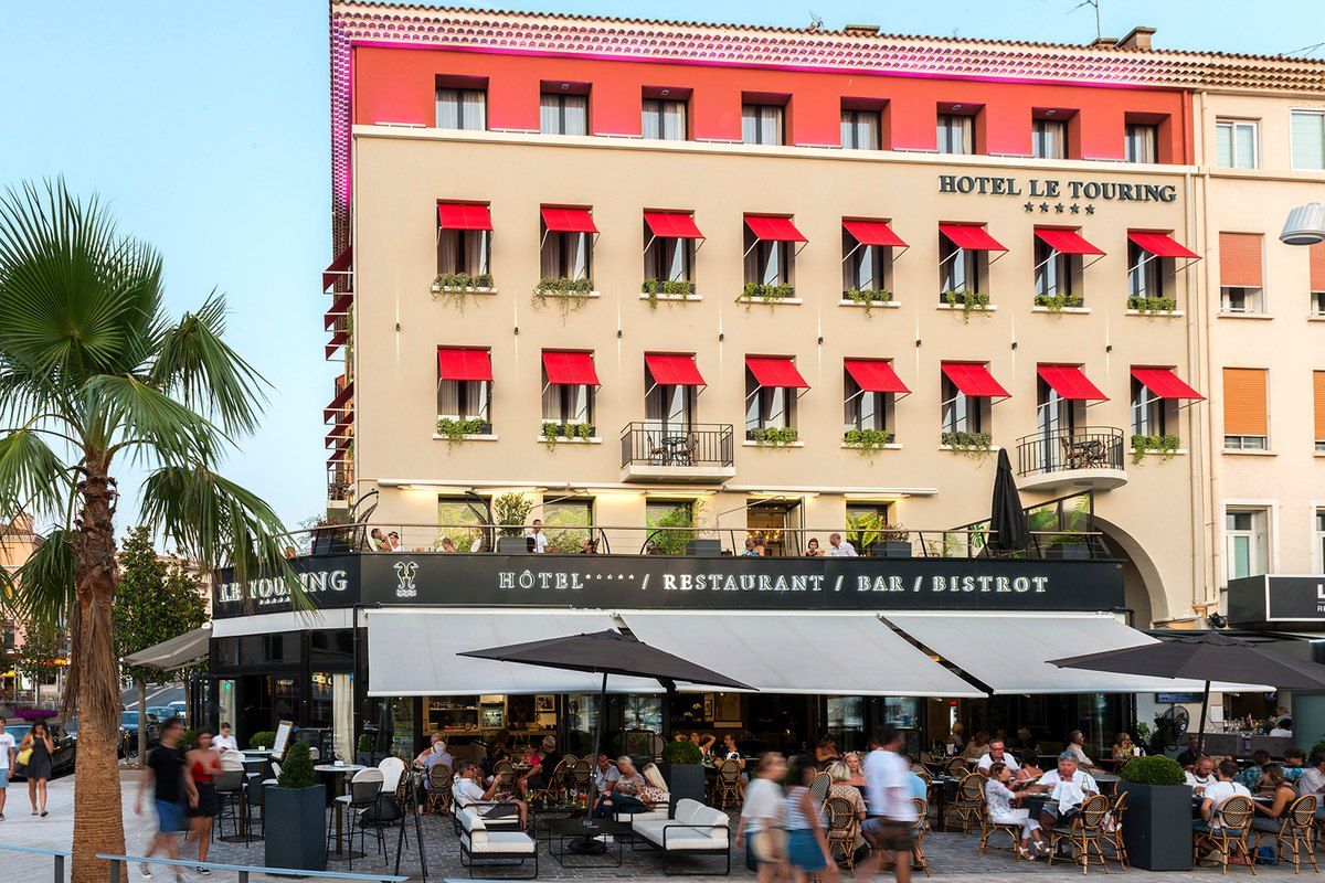 The pink-and-cream façade of the Hôtel Le Touring on the Old Port of Saint-Raphaël, with its bar terrace below