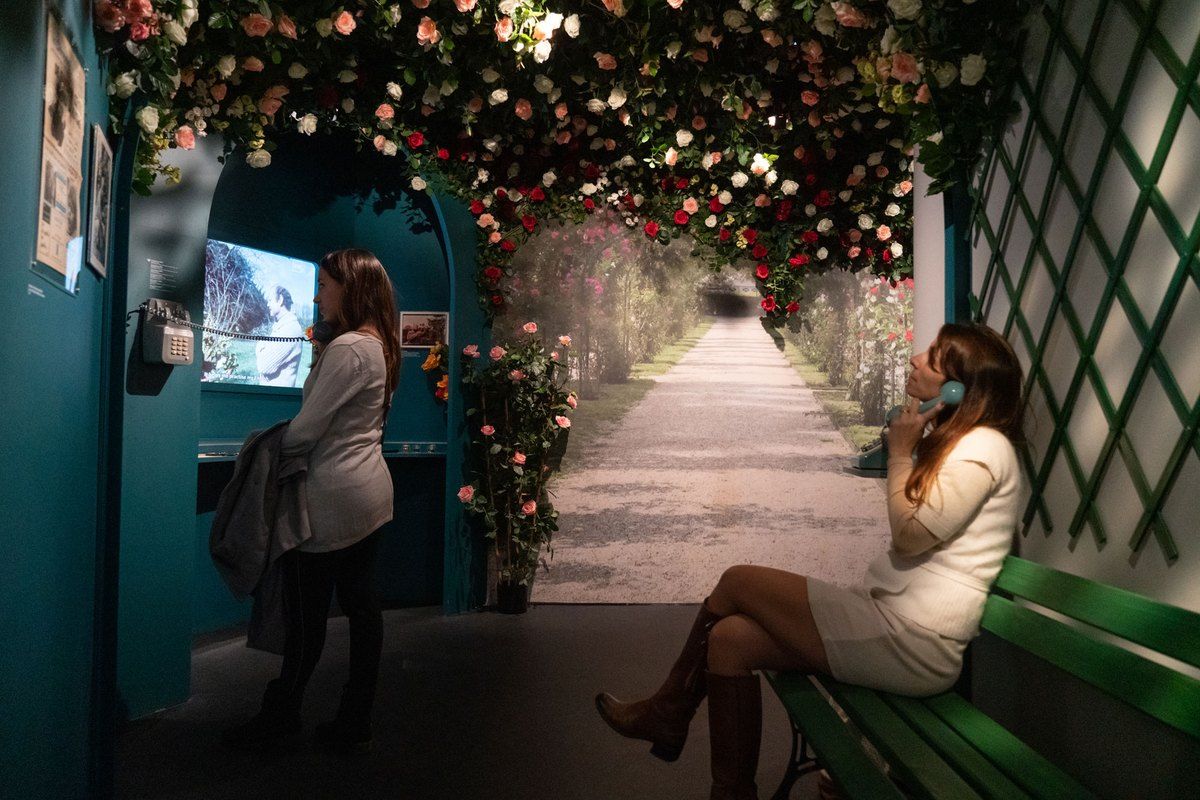 Inside the Musée Louis de Funès: a rose-covered arbour with a bench, telephones and screens playing film clips