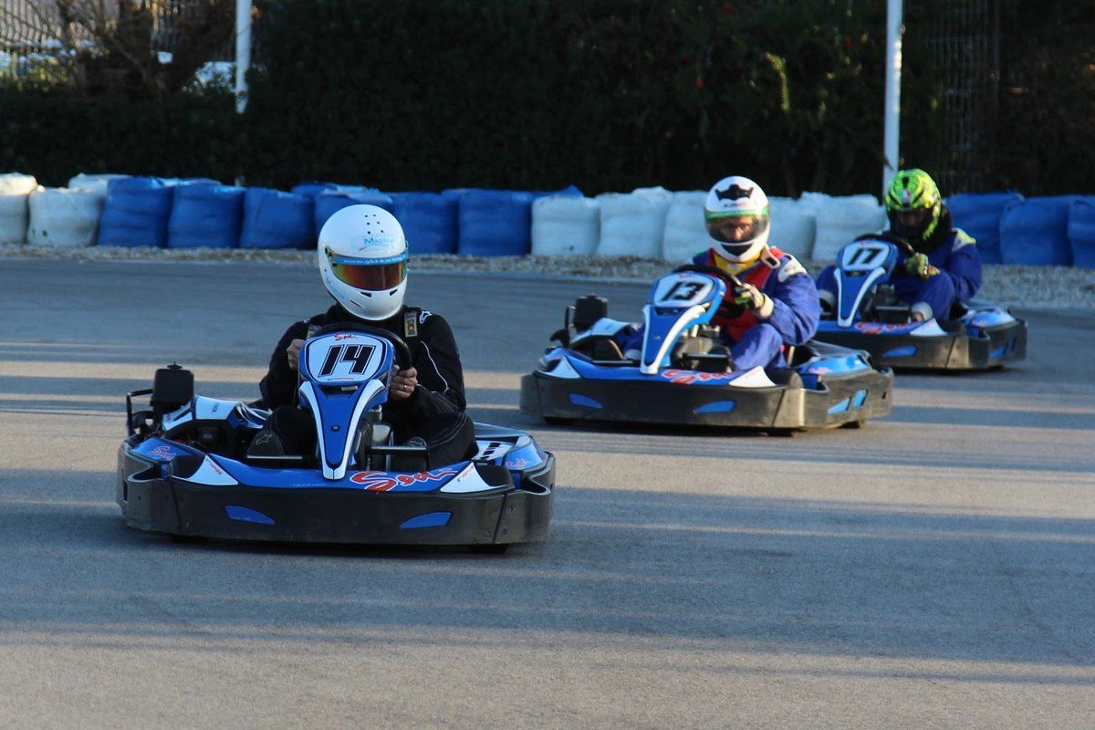 Three helmeted drivers racing go-karts on the track at Grimaud Karting Loisir
