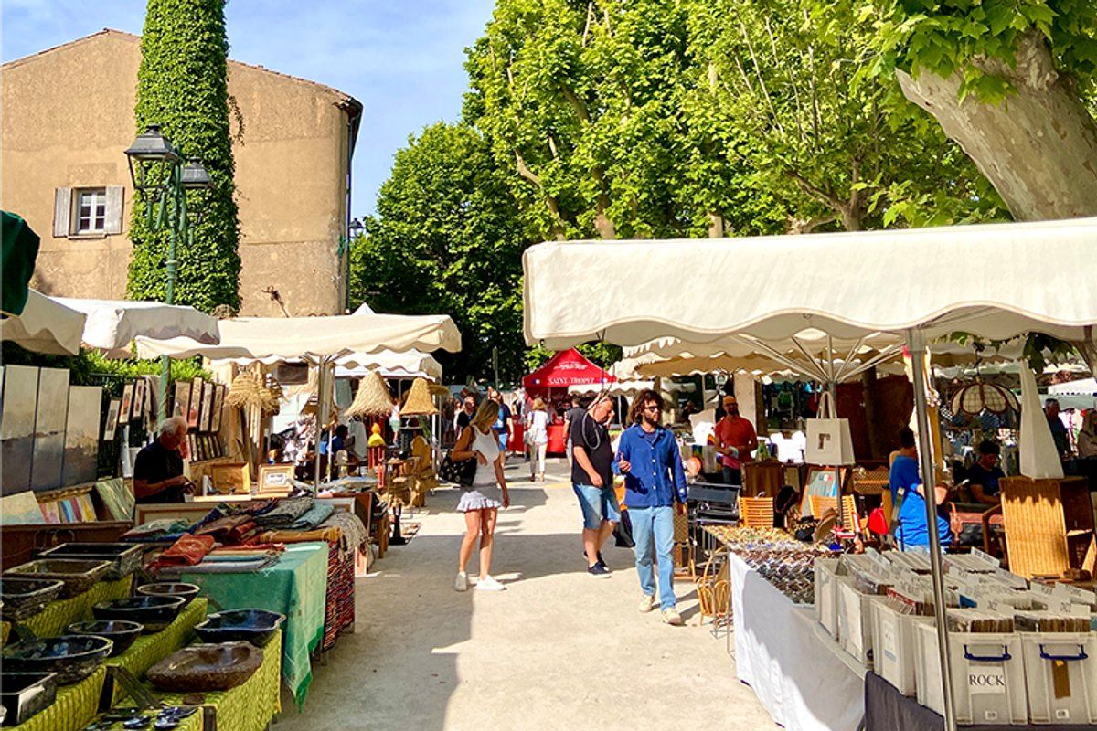 Market stalls and shoppers under white awnings on the Place des Lices, Saint-Tropez