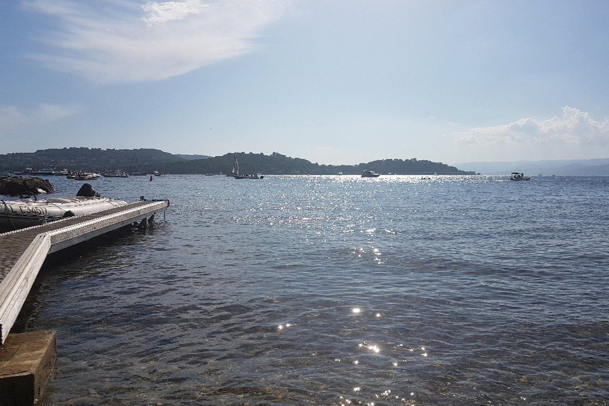 A wooden jetty over calm water at the Plage des Canoubiers, Saint-Tropez, with the Maures hills across the bay