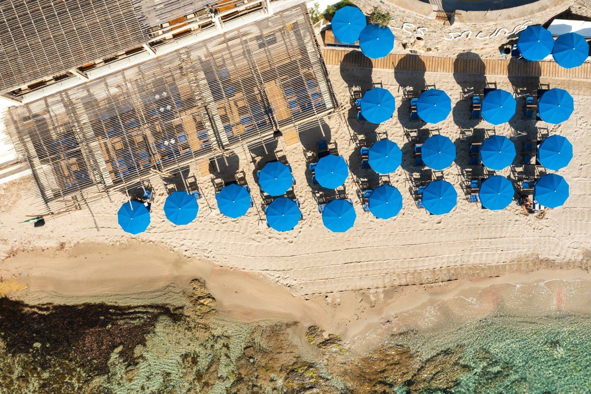 Aerial view of blue parasols on the sand and clear water at the Plage des Salins, Saint-Tropez