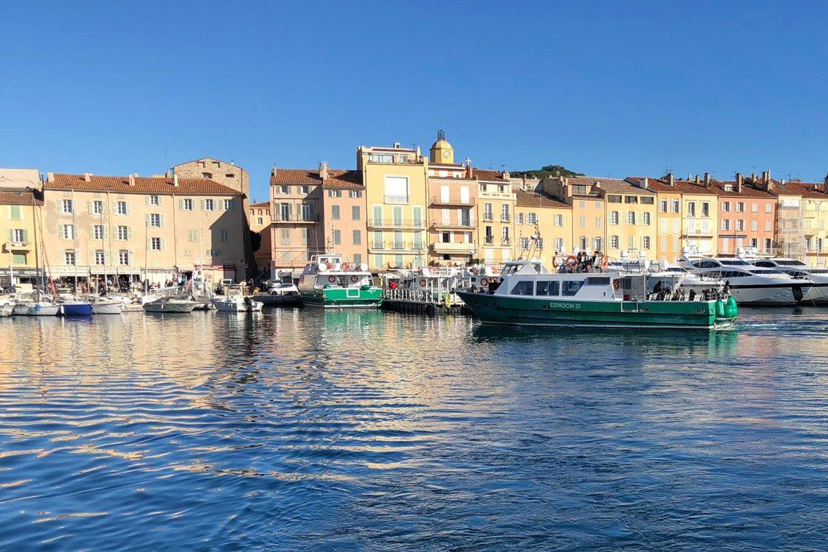 A green Bateaux Verts shuttle arriving in the harbour of Saint-Tropez, its pastel quayside houses behind