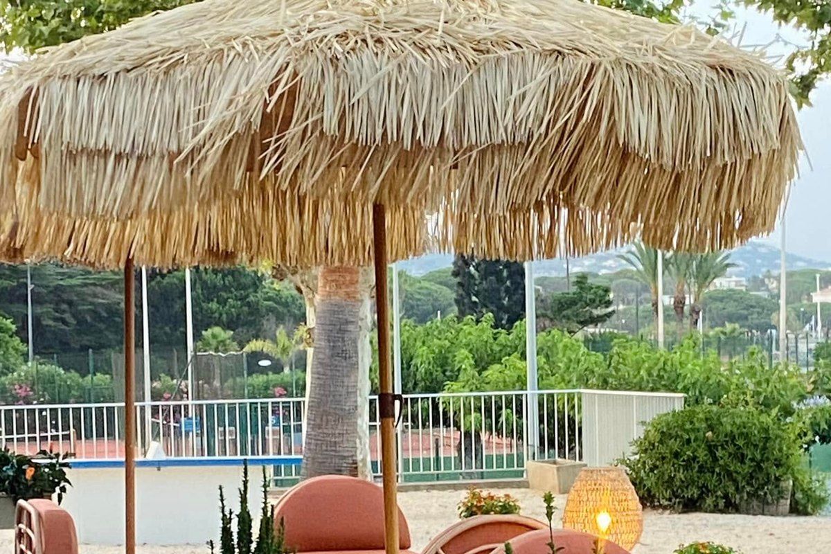 Terracotta armchairs under straw parasols on the deck of Café Croisette in Sainte-Maxime