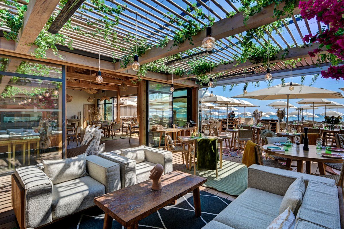 Sofas under a flowering pergola at La Voile on Nartelle beach, with the sea beyond
