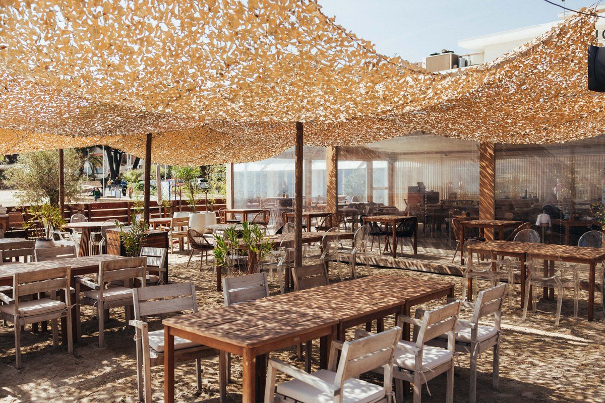 Wooden tables under a sand-coloured shade net on the terrace of Le Nino above the town beach