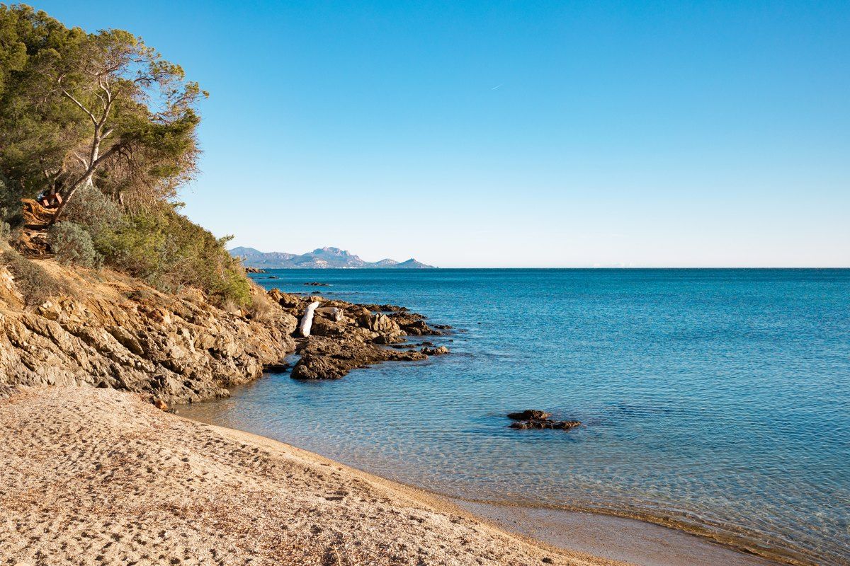 A small sandy cove below pines and ochre rocks on the coastal path of Les Issambres