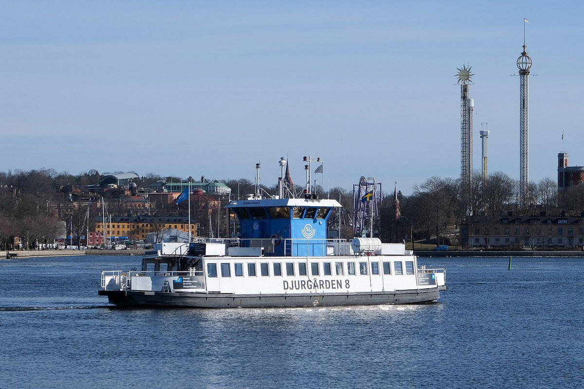 The blue-and-white Djurgården ferry on line 82 crossing the harbour, with Gröna Lund's towers behind
