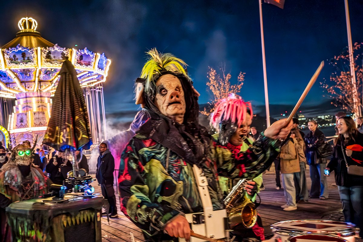 Costumed drummers in the Halloween parade at Gröna Lund at night, with the lit carousel behind