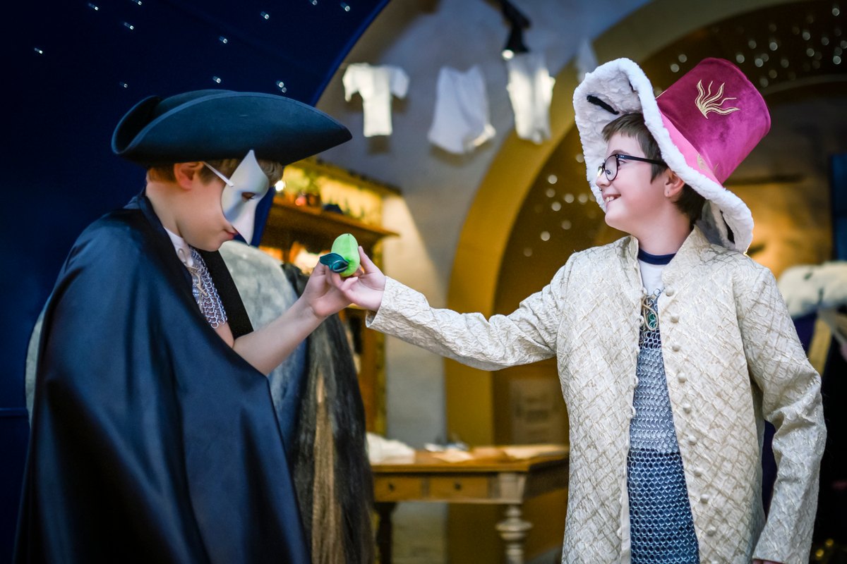 Two children dressing up in a tricorn hat, cloak and plumed hat under the starry ceiling of the Children's Armoury