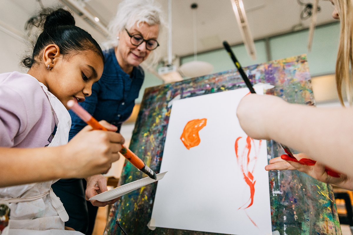 A girl and an older woman painting together on a shared canvas in the Workshop at Moderna Museet