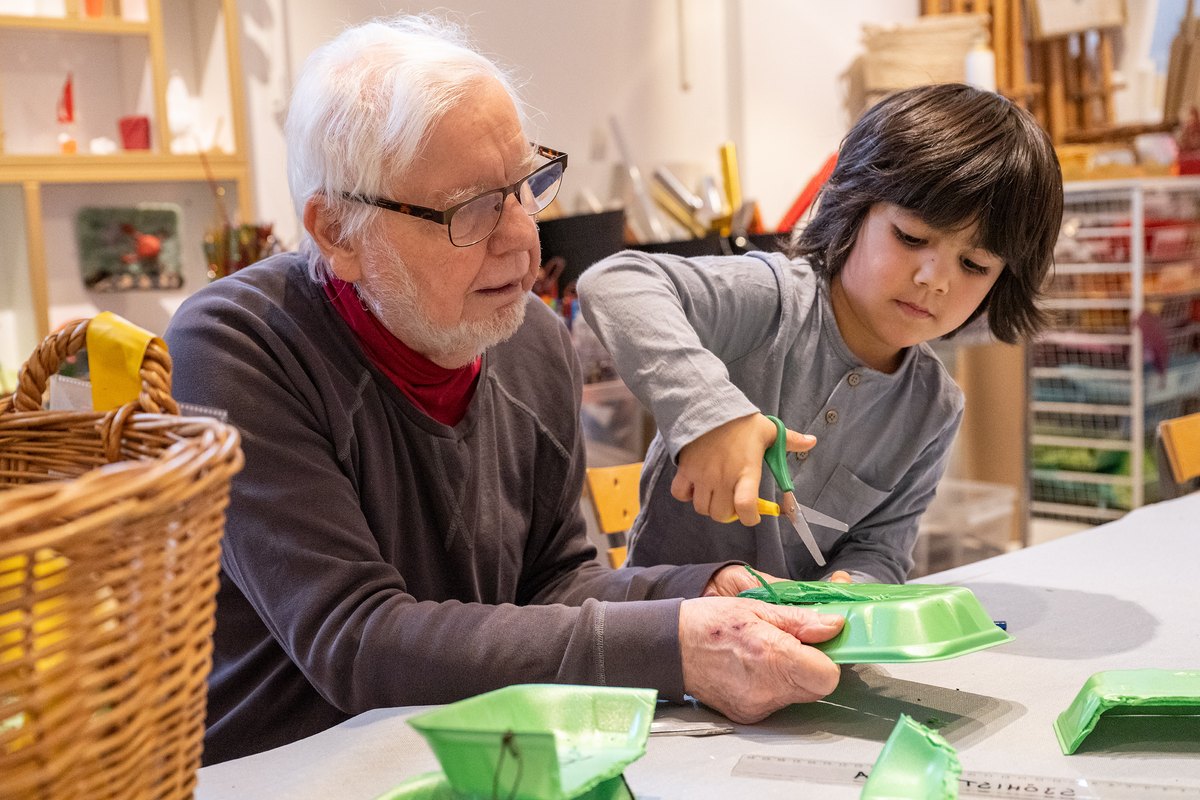 An older man and a boy cutting out and building boats together in the Ruskpricken workshop at Sjöhistoriska museet