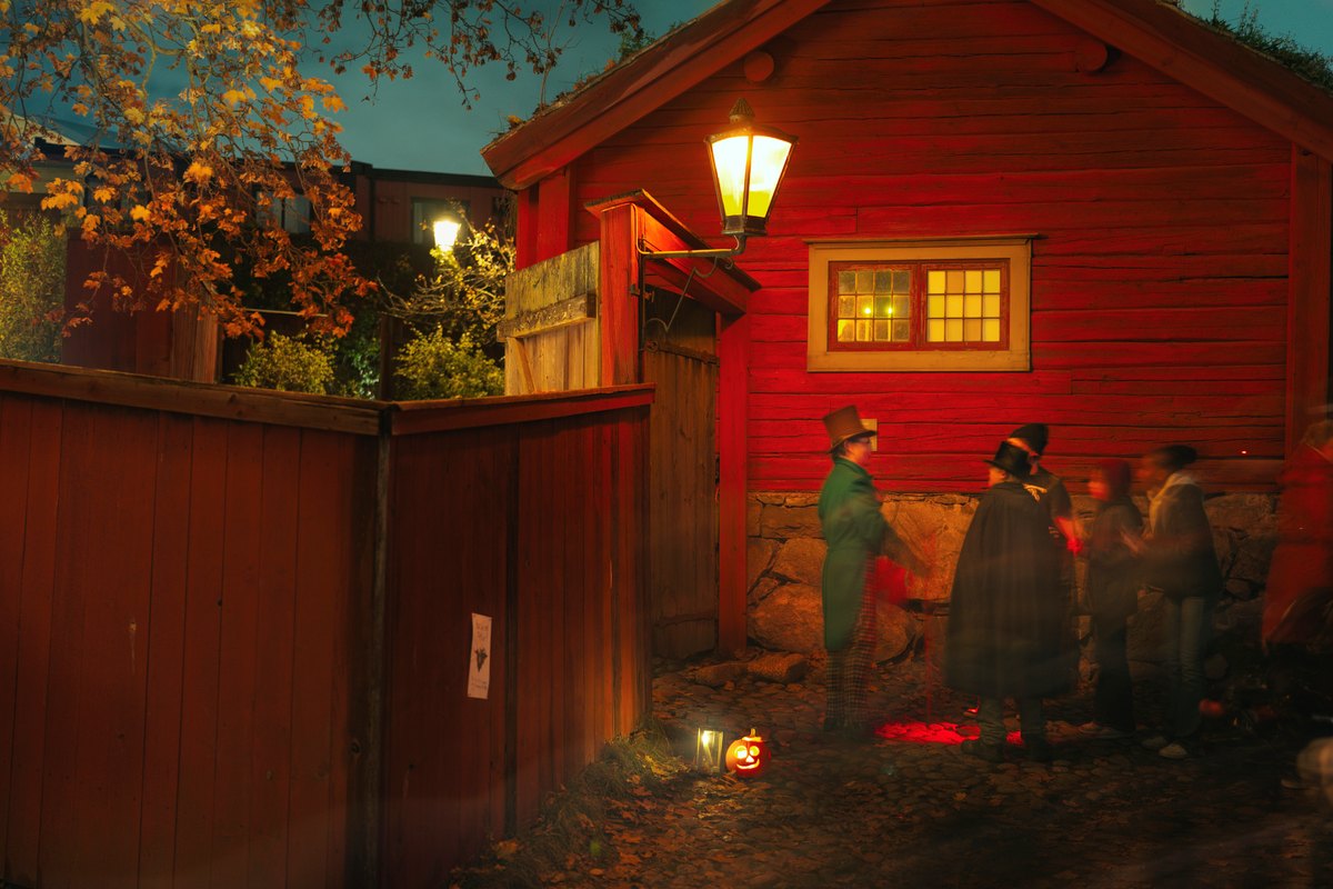 Costumed Halloween characters among the red wooden houses of Skansen's town quarter at dusk