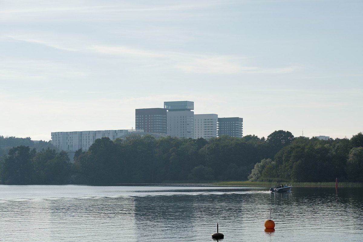 The still water of Årstaviken with the wooded Årsta holmar islands and the towers of Liljeholmskajen beyond
