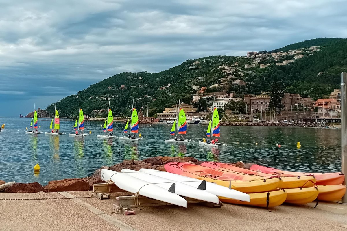Colourful sailing dinghies on the bay of Théoule and kayaks lined up on the shore of the Plage du Suveret