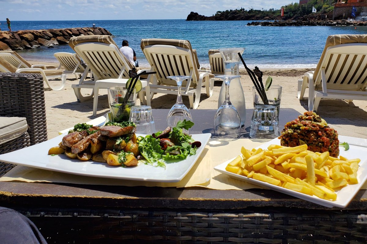 A plate of grilled meat with chips on a table by the sand at Le Panama, with loungers and the sea behind
