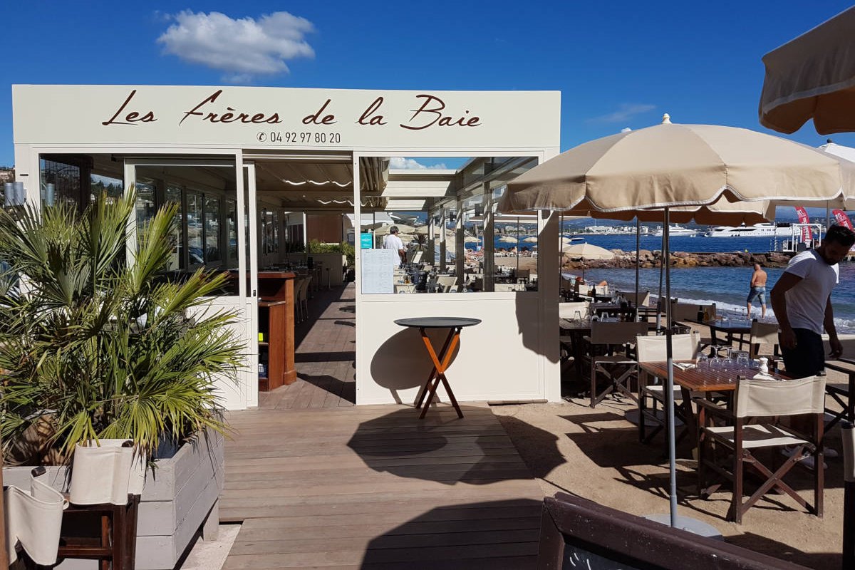 The white beach pavilion of Les Frères de la Baie with its wooden deck, parasols and palms
