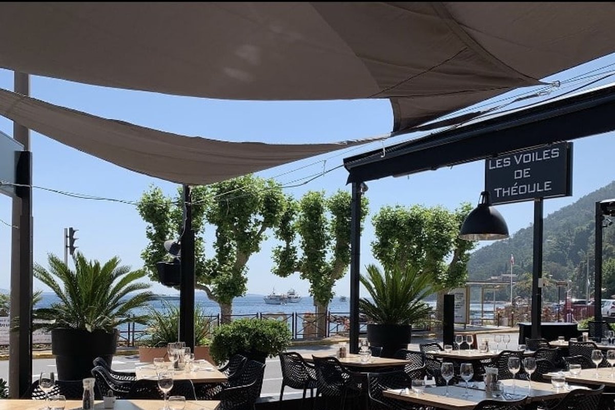 The shaded terrace of Les Voiles de Théoule under white sails, with palms and the restaurant's sign