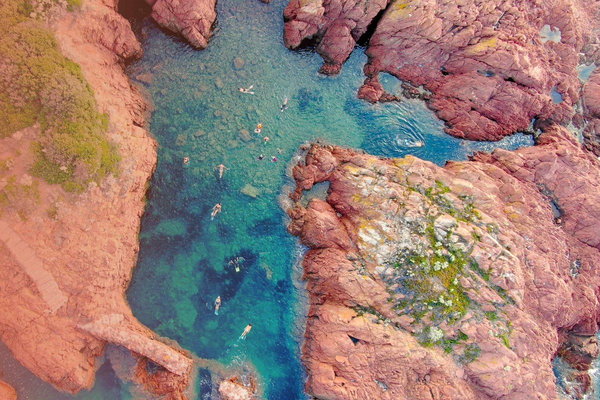 A red-rock cove of the Estérel seen from above, with swimmers in the clear green water