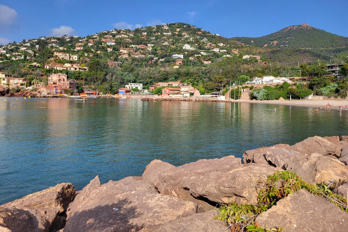 Calm water at La Figueirette, with red rocks in the foreground and villas on the green Estérel hillside