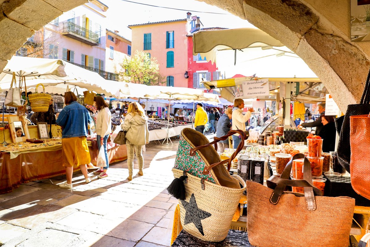 Market stalls seen through a stone arch on the Place des Arcades during Valbonne's Friday market