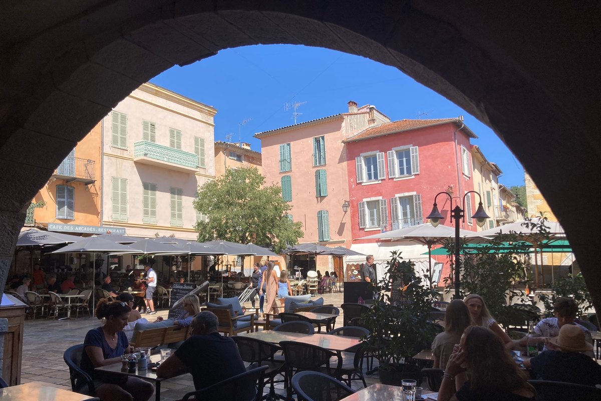 Café terraces on the Place des Arcades in Valbonne seen through one of its stone arches