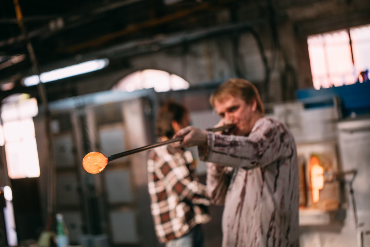 A glassblower turning a glowing gather of molten glass at La Verrerie de Biot
