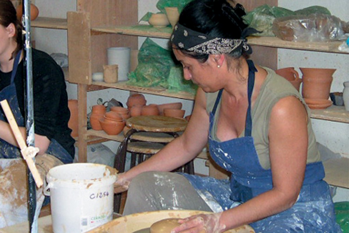 A student working clay at a bench in the workshop of the École d'Art Céramique de Vallauris, shelves of pots behind