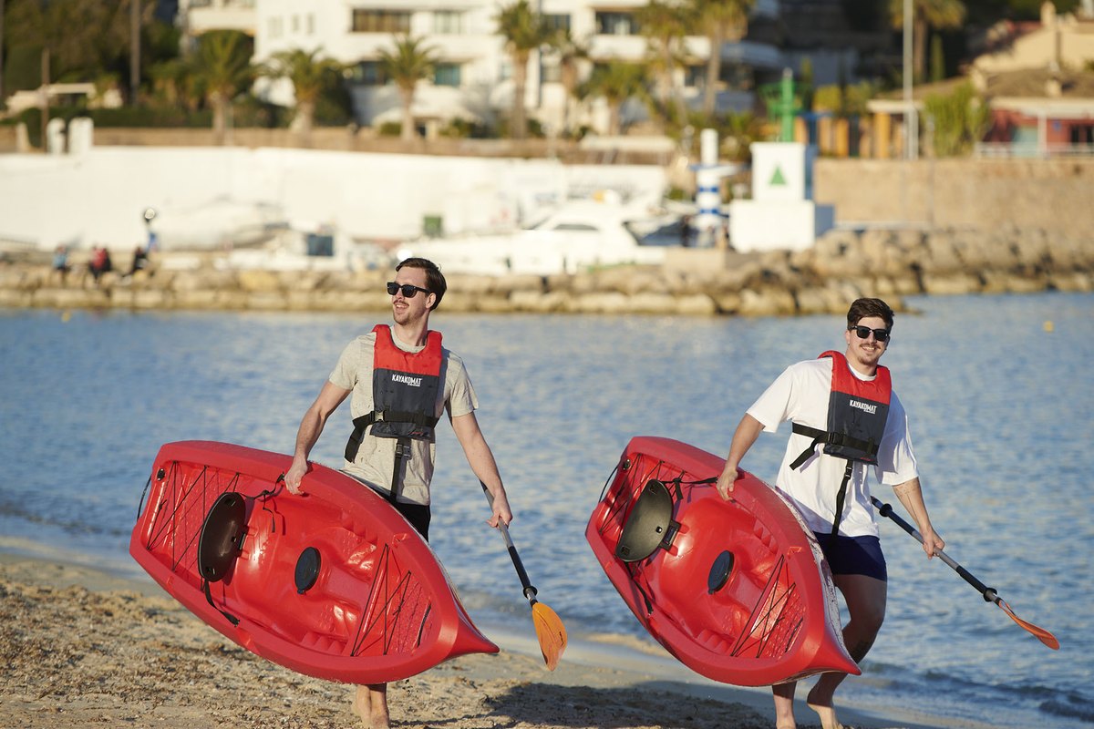 Two paddlers in life jackets carrying red sit-on kayaks down the sand at Golfe-Juan