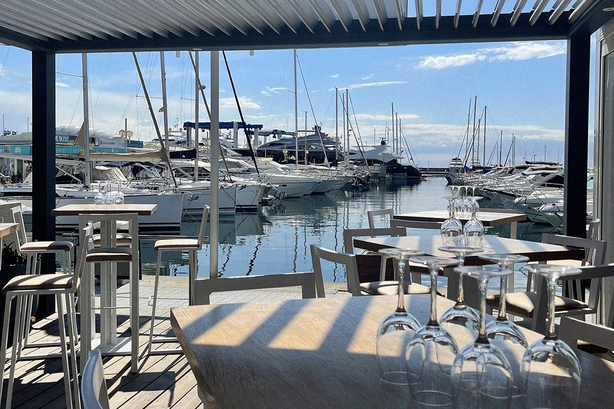 High tables under a pergola on L'Annexe's terrace, facing the masts of Port Camille Rayon