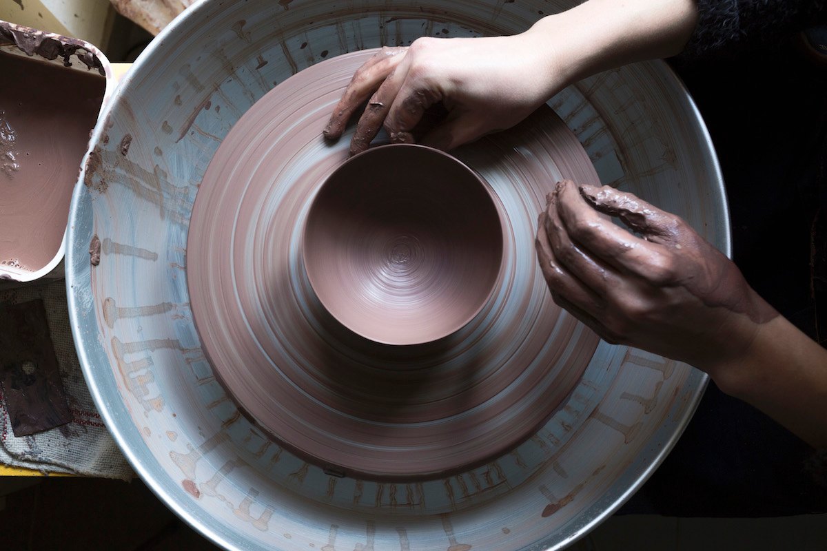 Hands shaping a bowl of red clay on the potter's wheel at Laurène Jeannette's ceramics studio in Vallauris