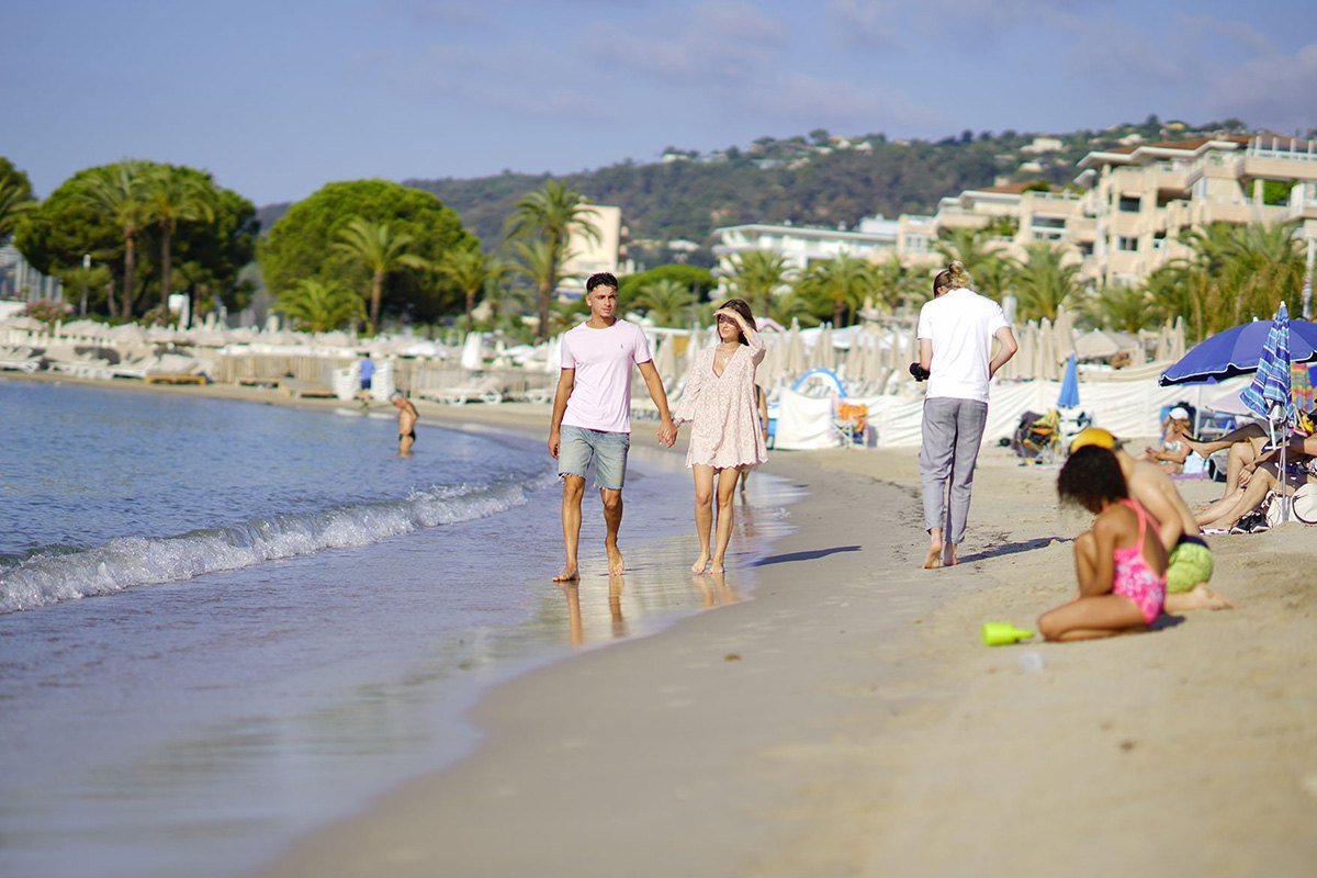 A family strolling and a child playing in the sand on the Plage du Midi at Golfe-Juan, pines and apartments behind
