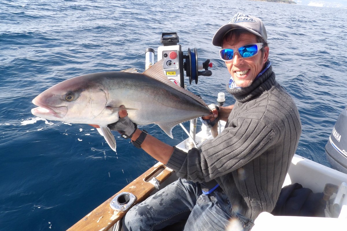 A fishing guide holding up a large amberjack on his boat off Golfe-Juan
