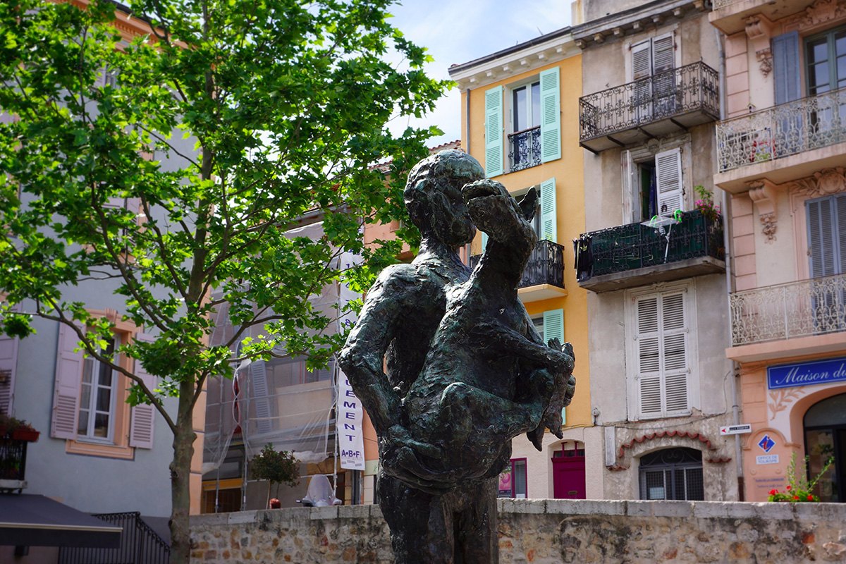 Picasso's bronze L'Homme au Mouton on its square in Vallauris, a plane tree and pastel façades behind