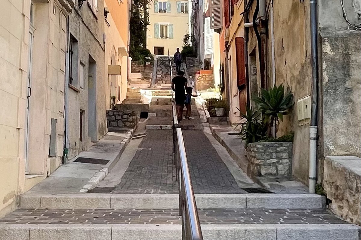 A stepped lane with a handrail climbing between old stone houses in Vallauris's old town