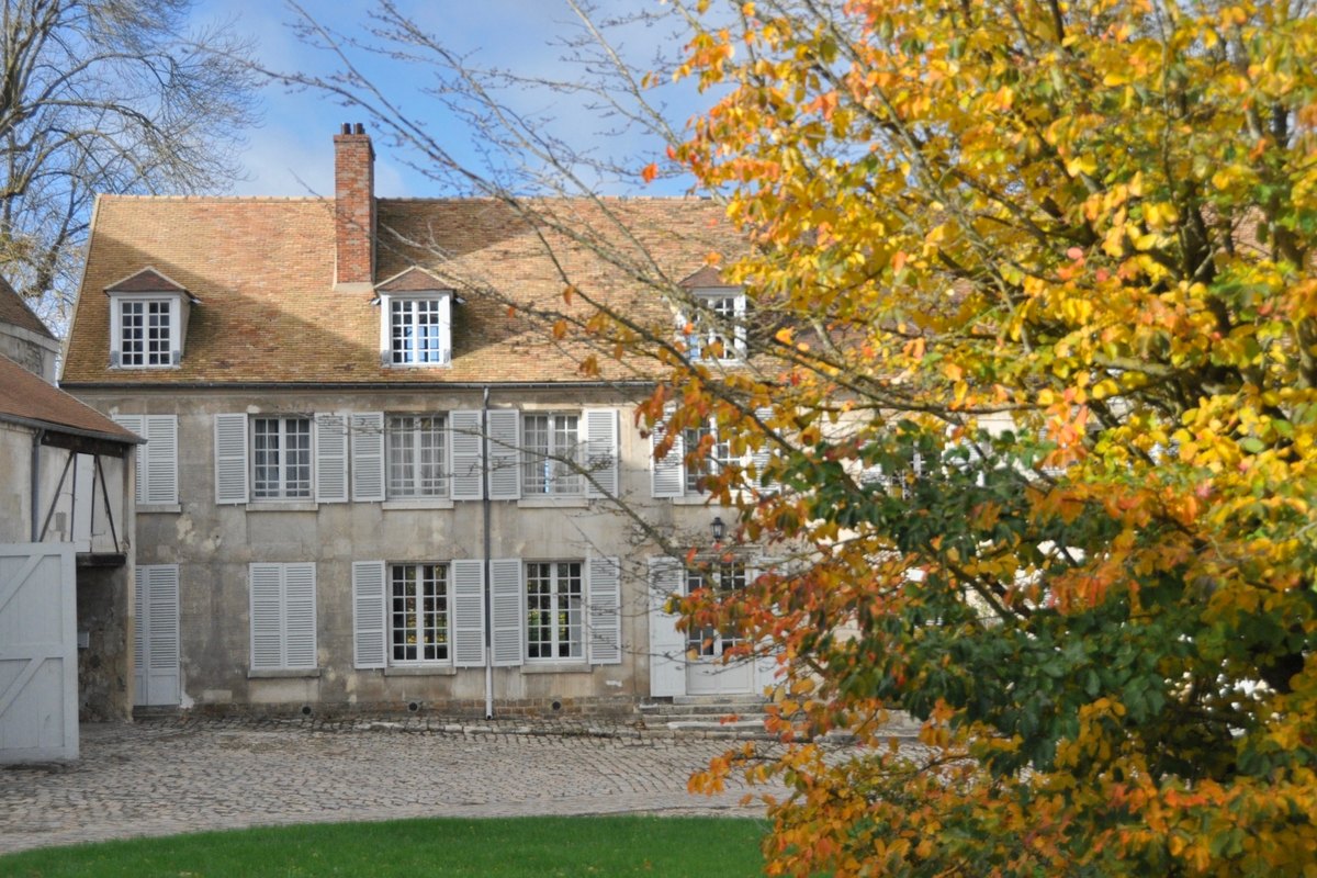 The old farmhouse of the Ferme de Gally at Saint-Cyr-l'École behind a tree in autumn colour