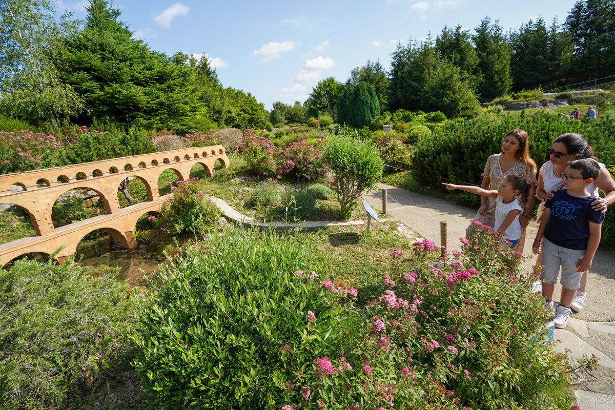 A family walking past the miniature Pont du Gard among flowering gardens at France Miniature, Élancourt