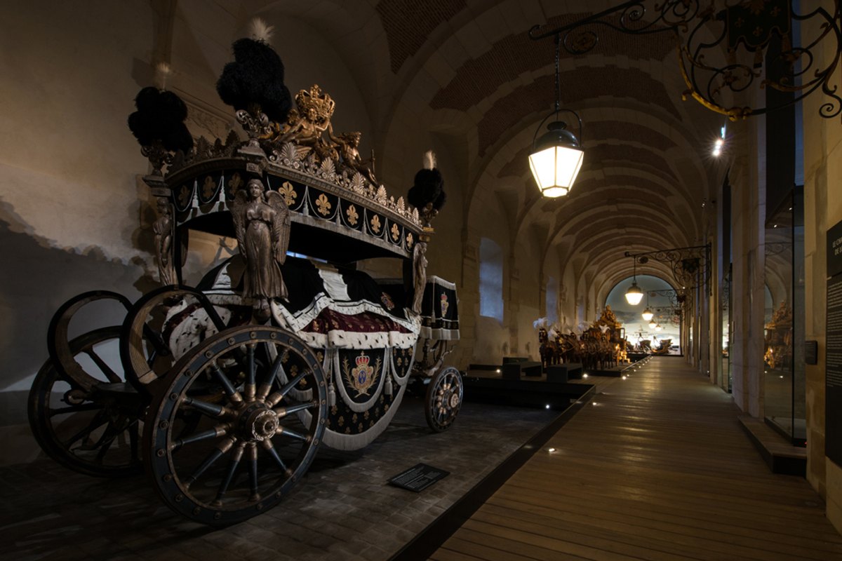 A gilded ceremonial coach under the vaulted ceiling of the Gallery of Coaches in the Great Stables, Versailles
