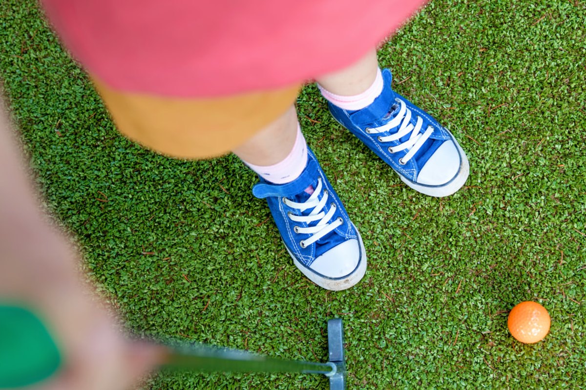 A child in blue trainers lining up a putt on the mini-golf course at the Île de loisirs de Saint-Quentin-en-Yvelines