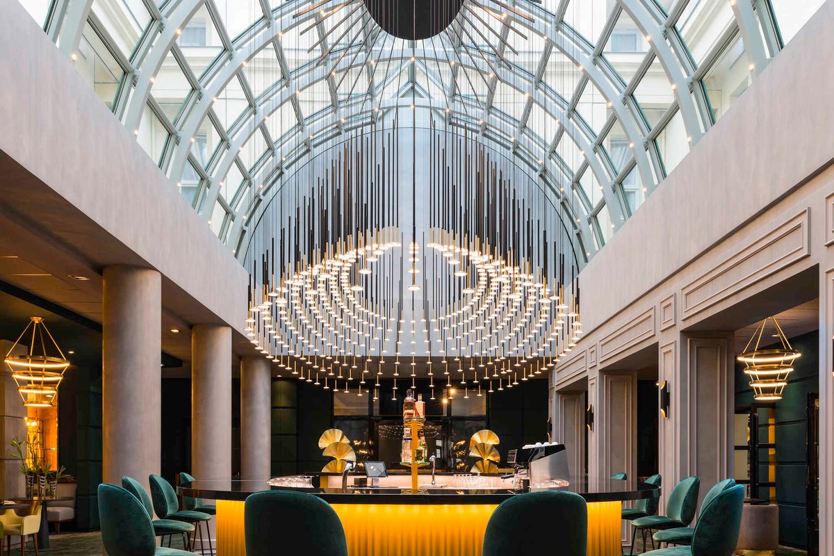 The glass-roofed L'Alcôve bar with its chandelier of lights at Le Louis Versailles Château – MGallery