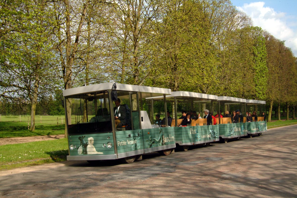 The little train of the Palace of Versailles running along a tree-lined avenue in the park