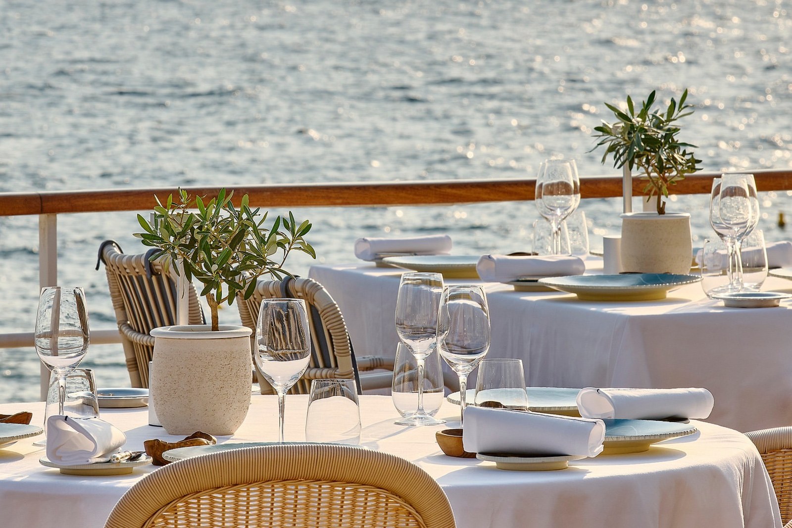 Tables laid with white cloths and potted olive trees on the Eden-Roc terrace at the Hôtel du Cap-Eden-Roc, with the sea behind