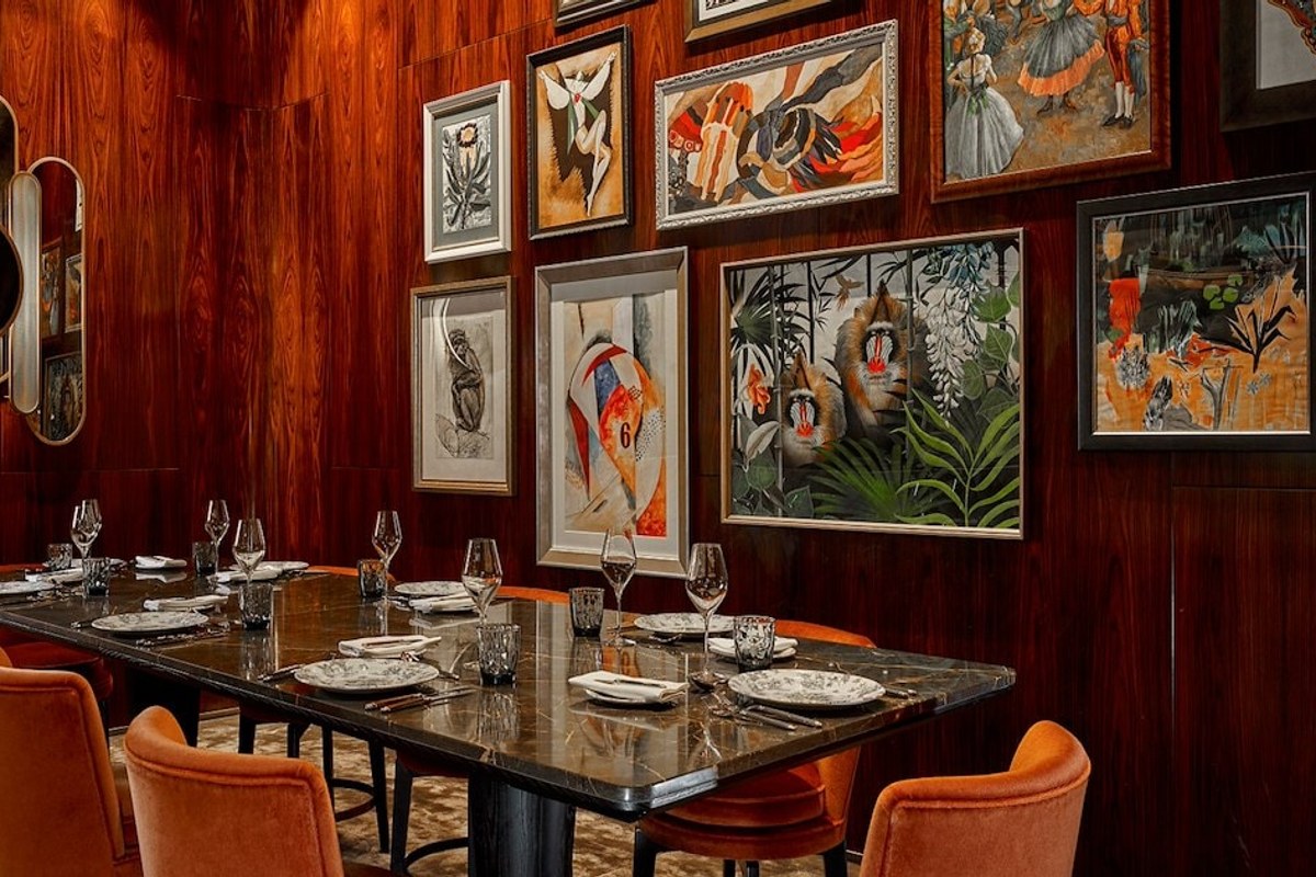 Private dining room with wood-paneled walls, gallery of framed art, set marble table with orange chairs