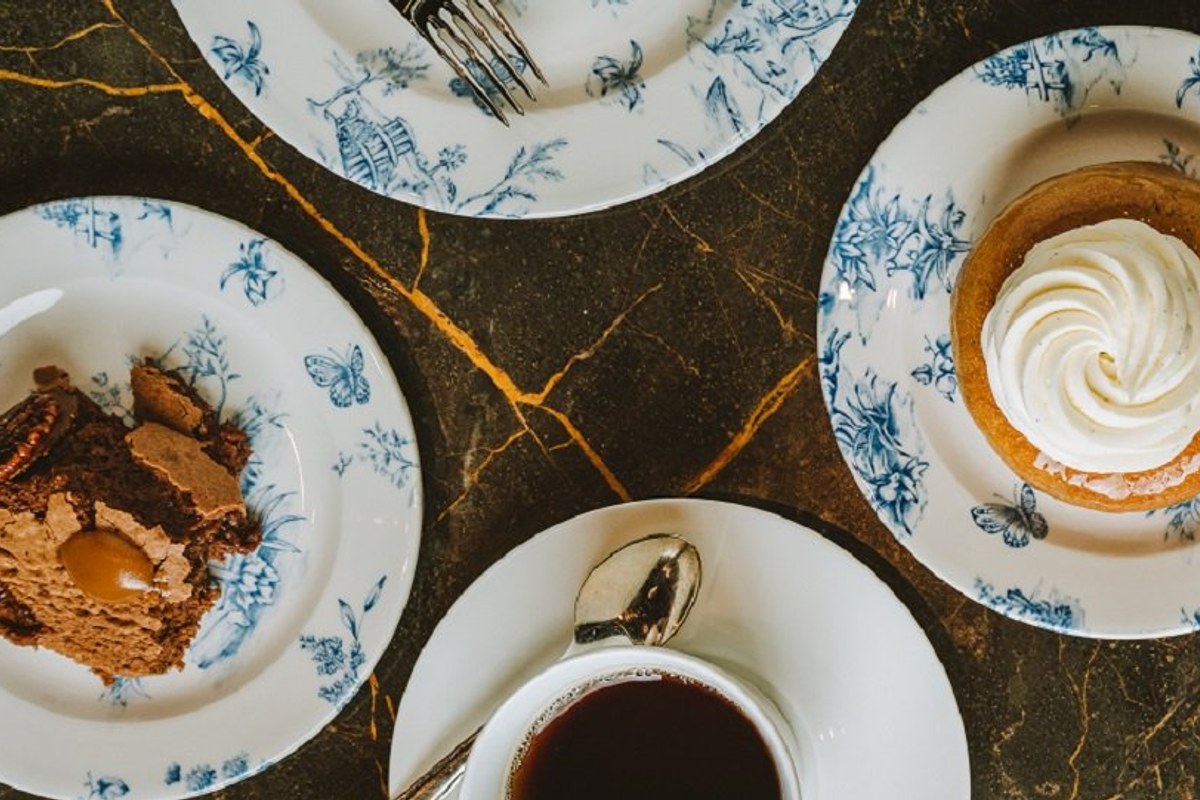 Overhead view of dessert plates with chocolate cake, coffee and tart on patterned blue and white china