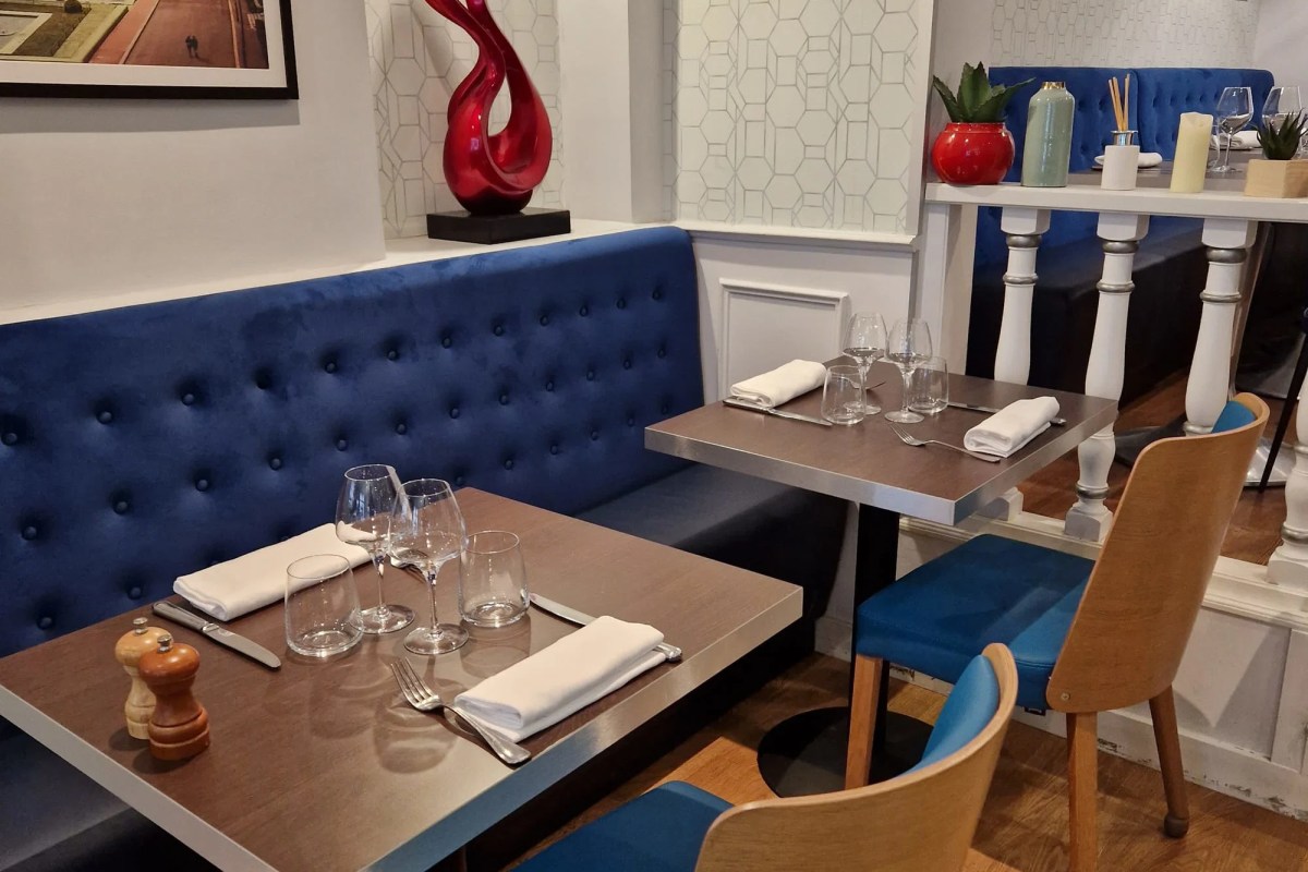 Restaurant dining room interior with blue tufted banquette seating, set tables with wine glasses and folded napkins