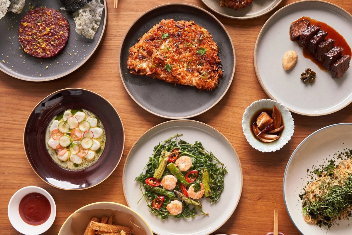 Overhead view of an assorted Korean-inspired tasting spread including tartare, rice cake, braised beef, shrimp and greens